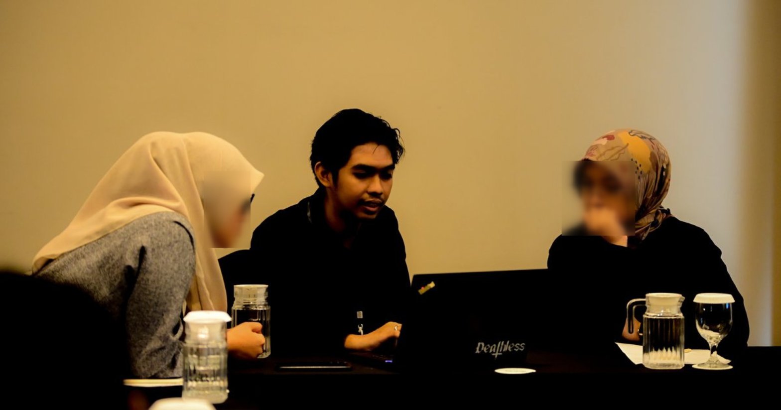 Three people talking at a table in the breakout room. The author sits in the middle and explains while two participants, faces blurred, listen.