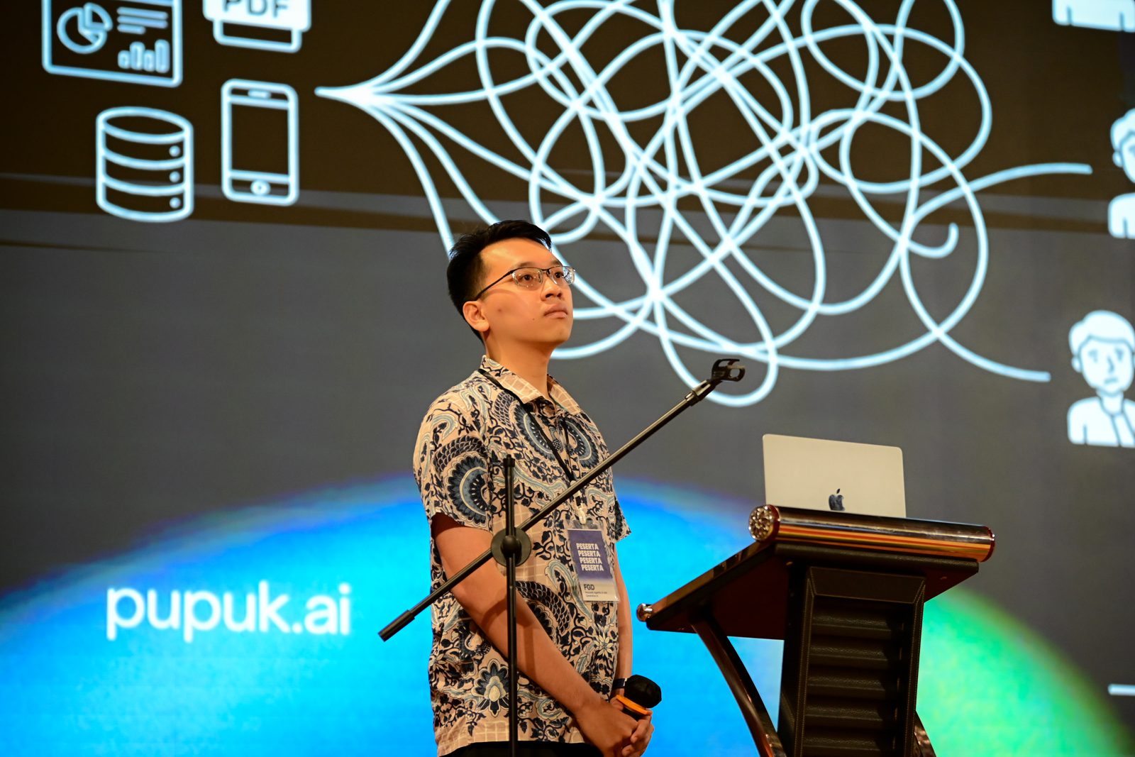 Windiarta on stage beside a podium, with a pupuk.ai slide behind him.