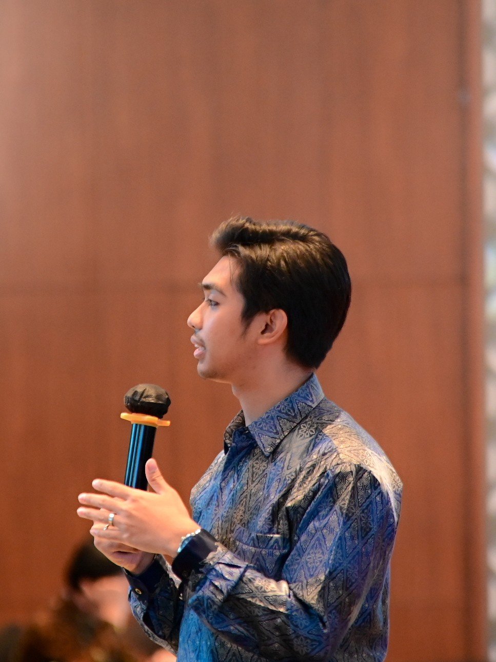The author, Aditya, in a blue batik shirt speaking into a microphone in the breakout room.