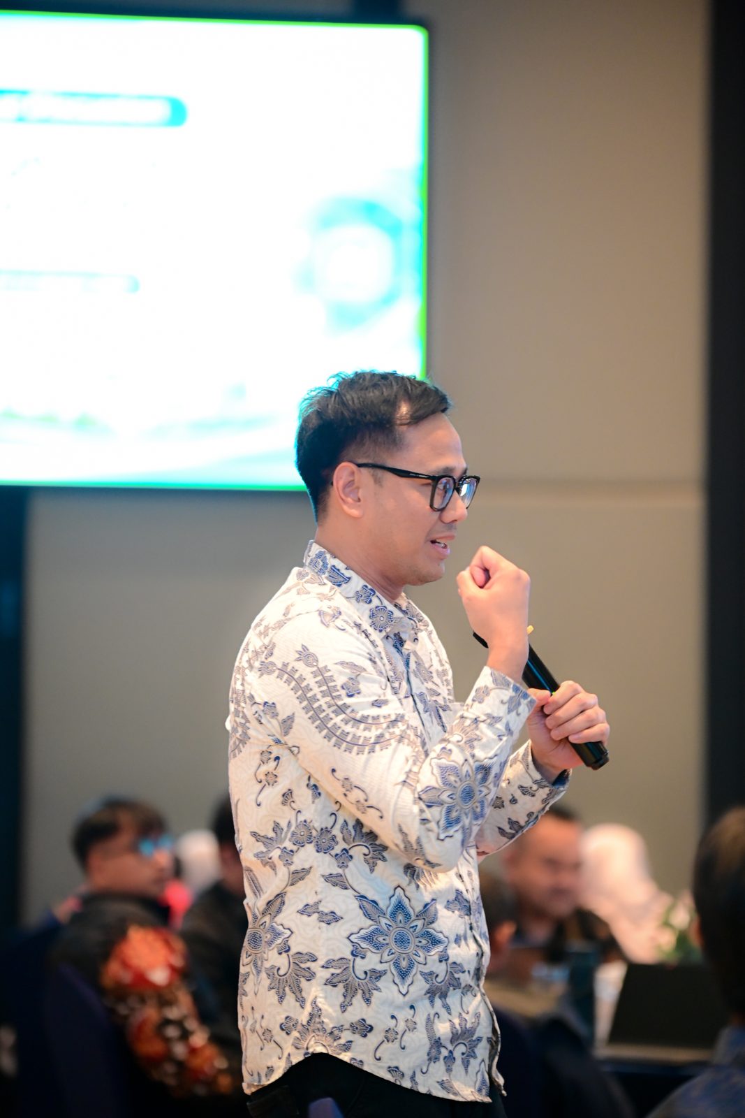 Dommy Asfiandy in a white batik shirt speaking into a microphone, explaining the layers of PINTER.
